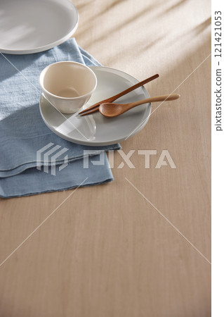 Various tableware on a soft wood-toned table background with sunlight shining through. Various tableware on a soft wood-toned table background with sunlight shining through. 121421053