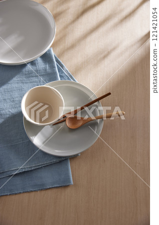 Various tableware on a soft wood-toned table background with sunlight shining through. 121421054