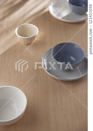 Various tableware on a soft wood-toned table background with sunlight shining through. Various tableware on a soft wood-toned table background with sunlight shining through. 121421056