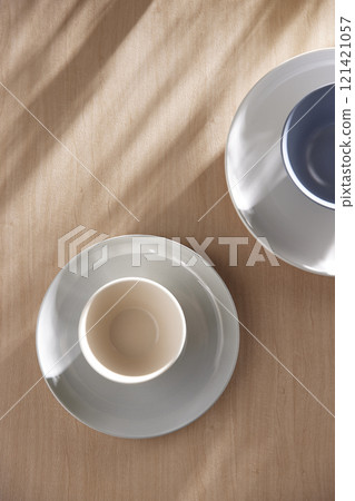 Various tableware on a soft wood-toned table background with sunlight shining through. Various tableware on a soft wood-toned table background with sunlight shining through. 121421057