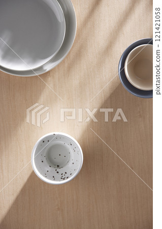 Various tableware on a soft wood-toned table background with sunlight shining through. Various tableware on a soft wood-toned table background with sunlight shining through. 121421058