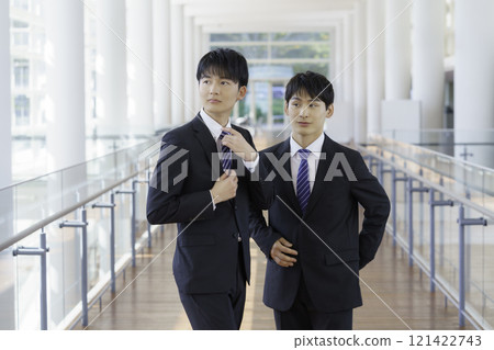 Two young businessmen walking down the corridor of an office building 121422743