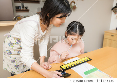 An elementary school student using an abacus and his mother checking the answers 121423530