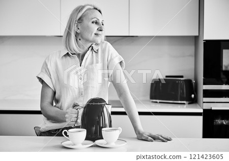 Pretty female making tea for two. Young woman holding kettle and brewing tea. Beautiful woman looking away and smiling. Black and white image. 121423605