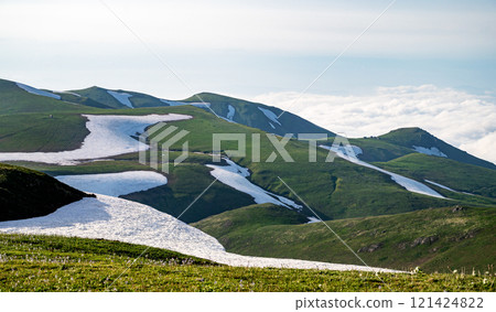 Green mountains with melting snow and fresh grass under cloudy sky. Green mountains with melting snow and fresh grass under cloudy sky. 121424822