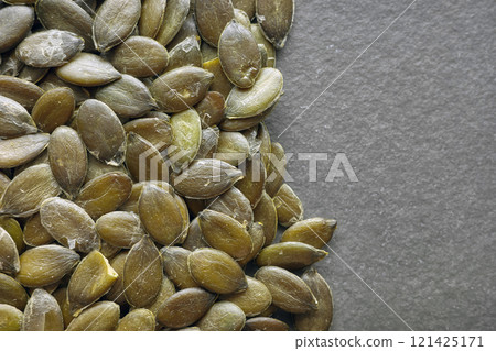 Close up photo of organic pumpkin seeds on a dark slate background, selective focus. Close up photo of organic pumpkin seeds on a dark slate background, selective focus. 121425171