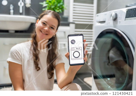 Young woman using mobile phone control via wi-fi and app for washing machine in home. Homesmart and new technology concept Young woman using mobile phone control via wi-fi and app for washing machine in home. Homesmart and new technology concept 121430421
