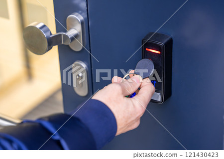 Close up view of person using a electric lock key fob to access a building via a reader of entry system mounted on a house wall 121430423