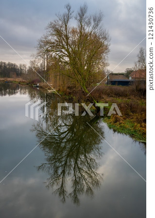 A tree gives a beautiful reflection in a river. A dark sky with clouds in the background A tree gives a beautiful reflection in a river. A dark sky with clouds in the background 121430736
