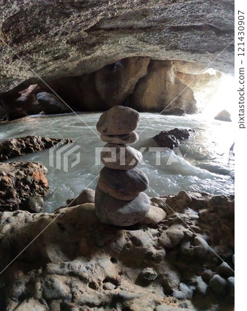 Balancing stones in a cave with stone arches against a white water river 121430907