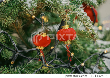 Close-up of green Christmas tree with mini red lanterns and festive lights, Chinese and Western holiday traditions Close-up of green Christmas tree with mini red lanterns and festive lights, Chinese and Western holiday traditions 121432498