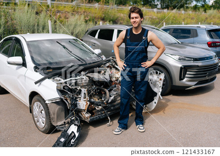 Portrait of mechanic male carefully inspecting damaged car in salvage yard, demonstrating care and accountability in automobile repair and renew service station. Concept of professional car repair. 121433167