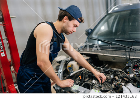 Muscular automotive mechanic male check up engine of old car. Serious vehicle service manager worker work in mechanics garage, check and maintenance to repair motorcar car in workshop. Muscular automotive mechanic male check up engine of old car. Serious vehicle service manager worker work in mechanics garage, check and maintenance to repair motorcar car in workshop. 121433168