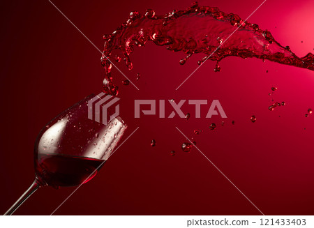 Glass and red wine splash on a dark red background. 121433403
