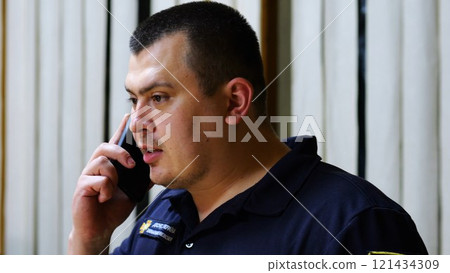 Male firefighter chief have serious telephone conversation with his subordinate by smartphone at fire station. Nervous fireman talking by mobile phone at fire department. Concept of heroic profession 121434309
