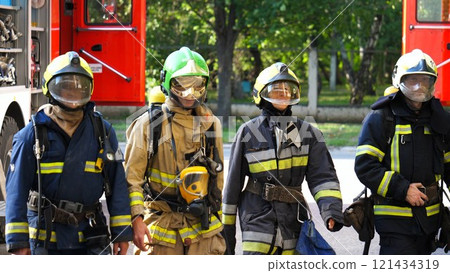 Tired male and female fireguards in full equipment walk after putting out the fire. Young exhausted firemen and firewoman go after extinguishing emergency. Saving lives and heroic profession concept 121434319