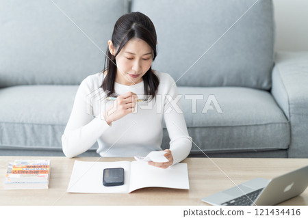 A middle-aged woman writing a book with a receipt in one hand 121434416