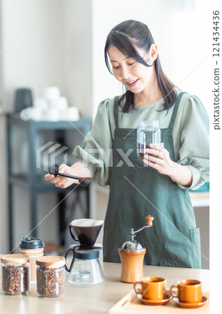 A middle-aged woman pouring coffee beans into a dripper at a cafe 121434436