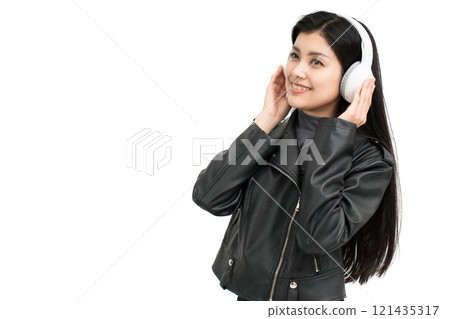 Young woman wearing a leather jacket listening to music on headphones 121435317