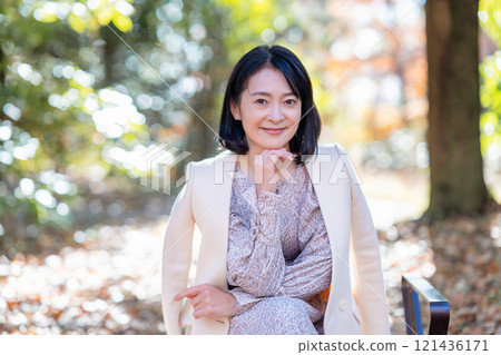 中年婦女坐在充滿自然的公園的長凳上 121436171