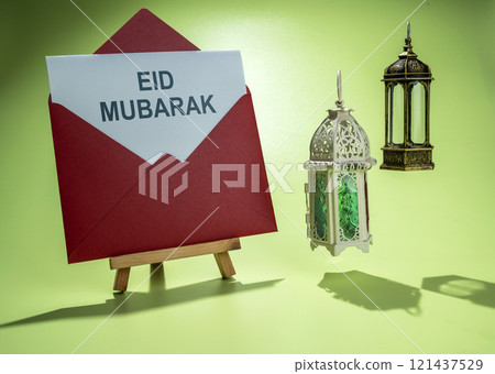 Wooden easel and envelope with the text of Eid Mubarak and Arabic lanterns hanging on a colored background Wooden easel and envelope with the text of Eid Mubarak and Arabic lanterns hanging on a colored background 121437529
