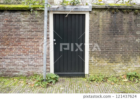 The facade of the black door between a brick wall with a green bush around it The facade of the black door between a brick wall with a green bush around it 121437624