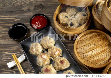Assorted chinese dim sum dumpling on the plate with bamboo wooden basket bowl and chopstick with sauce on wooden table 121437659