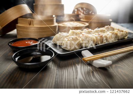 Assorted chinese dim sum dumpling on the plate with bamboo wooden basket bowl and chopstick with sauce on wooden table 121437662