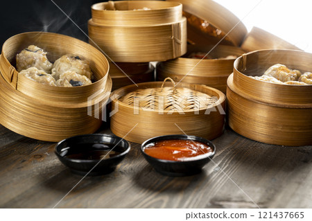 Assorted Chinese dim sum dumplings on the wooden basket bowl with sauce and soy sauce on the wooden table 121437665