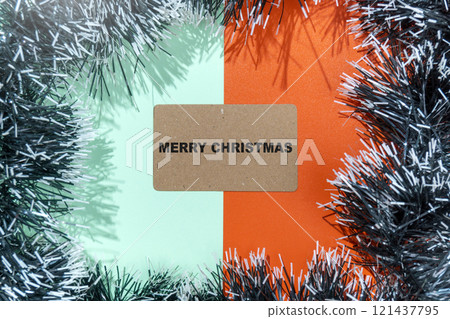 Closeup view of Merry Christmas text on a brown card with a Christmas ornament frame on a colored background 121437795
