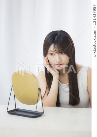 A young woman looks in the mirror and worries about her skin 121437987