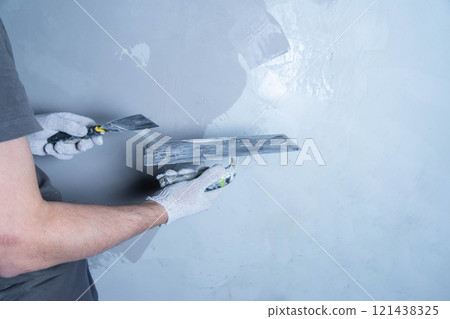 A person applies microcement to a wall surface with a putty knife in a workshop. A person applies microcement to a wall surface with a putty knife in a workshop. 121438325