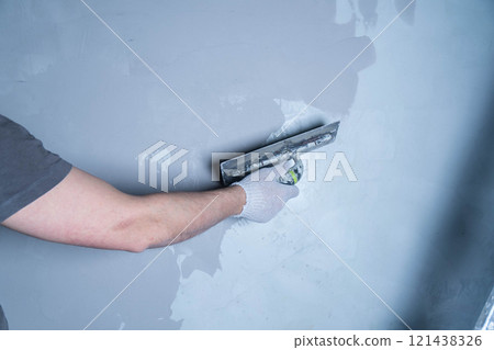 A worker uses a trowel to apply microcement adhesive to repair a wall in a residential area. A worker uses a trowel to apply microcement adhesive to repair a wall in a residential area. 121438326