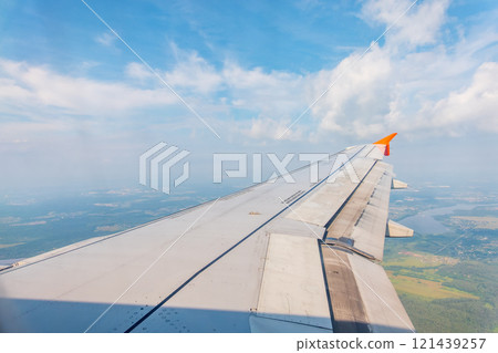 View of airplane wing, blue skies and green land during landing. Airplane window view. View of airplane wing, blue skies and green land during landing. Airplane window view. 121439257
