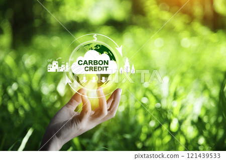 Carbon Credit Market and Net Zero. Carbon credit icon in hand on nature green background. There is increased investment in carbon trading markets. Environmental protection, energy neutral. Carbon Credit Market and Net Zero. Carbon credit icon in hand on nature green background. There is increased investment in carbon trading markets. Environmental protection, energy neutral. 121439533
