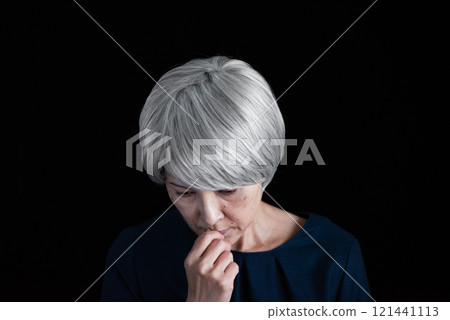 A senior woman with grey hair looking down sadly 121441113