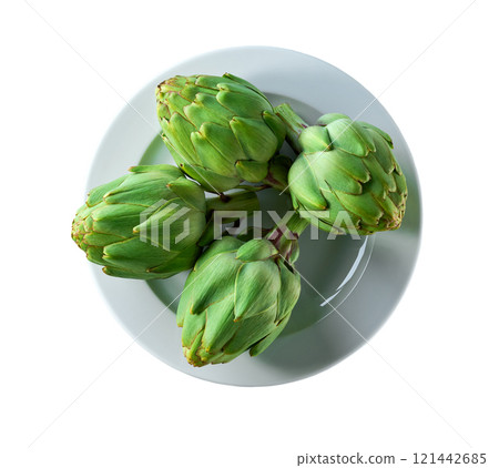 Green artichoke flower edible buds in a ceramic plate isolated on a white background. Top view. Green artichoke flower edible buds in a ceramic plate isolated on a white background. Top view. 121442685