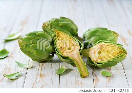 Fresh raw artichokes halved and ready for cooking on a wooden table. 121442723