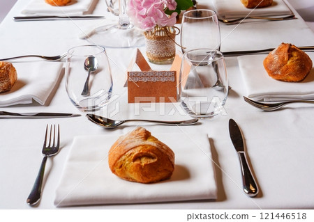 Elegant table setting with bread rolls and pink flowers centerpiece 121446518