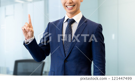 A smiling male businessman pointing with his index finger up A smiling male businessman pointing with his index finger up 121447499