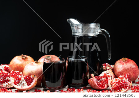 Pomegranate juice in jug and glasses among pomegranates, black background. Pomegranate juice in jug and glasses among pomegranates, black background. 121448503