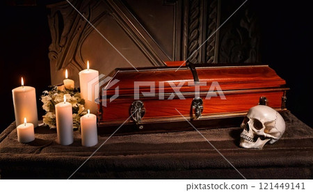 A solemn scene shows a coffin on a dark table, illuminated by candles and a skull 121449141