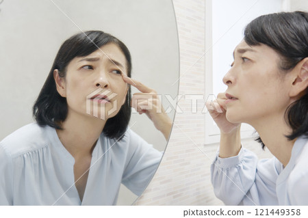 A woman in her 50s worries about the corners of her eyes in the mirror 121449358