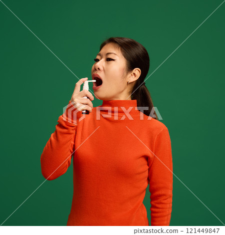 Woman using throat spray to ease pain and irritation caused by viruses or bacterial infections. Depicts home healthcare treatment for sore throat relief. Woman using throat spray to ease pain and irritation caused by viruses or bacterial infections. Depicts home healthcare treatment for sore throat relief. 121449847