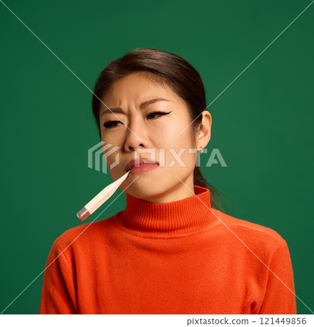 portrait of Asian woman holding thermometer in mouth, showing signs of fever or viral illness, common symptom during flu or cold infections. portrait of Asian woman holding thermometer in mouth, showing signs of fever or viral illness, common symptom during flu or cold infections. 121449856