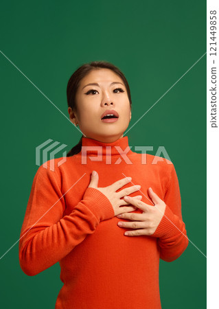 Asian woman with hands on chest, showing shortness of breath or chest discomfort, symptoms often caused by viral infections or respiratory distress. 121449858