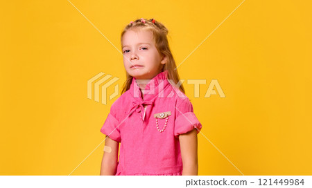 Portrait of scared girl in pink dress tearfully glancing, nervous after vaccination against yellow studio background. Portrait of scared girl in pink dress tearfully glancing, nervous after vaccination against yellow studio background. 121449984