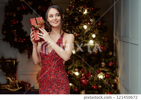 Woman in Festive Red Dress Holding Gift Box. 121450672