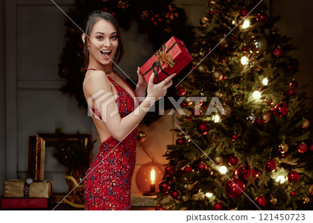 Excited Woman Holding Festive Gift Box Near Christmas Tree. 121450723