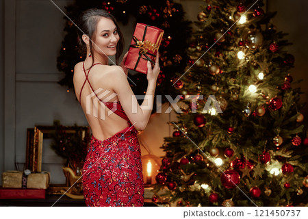 Smiling Woman in Red Gown Holding Christmas Present. 121450737